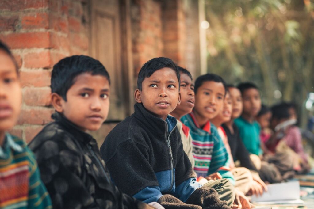 Mastering the First Impression: Your intriguing post title goes here A group of children from Bangladesh sitting outdoors, engaged in learning at a rural school.