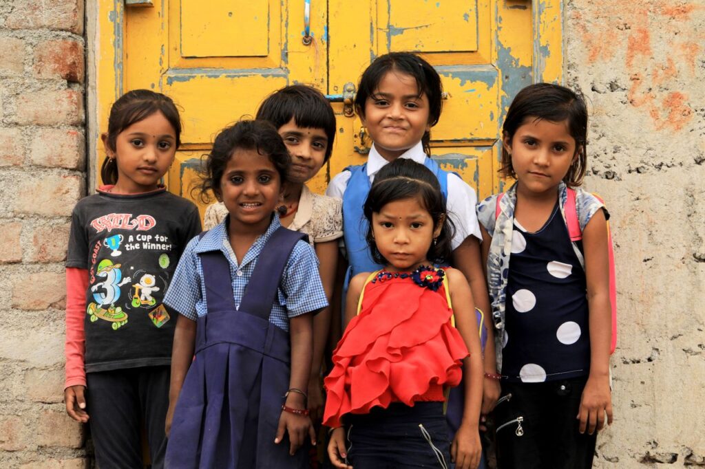 Crafting Captivating Headlines: Your awesome post title goes here A group of six South Asian children smiling and posing together in front of a colorful old door.
